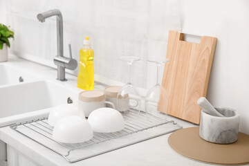 Drying rack with clean dishes near sink in stylish kitchen