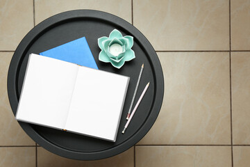 Notebooks, pencils and decorative holder with candle on round table indoors, top view. Space for text