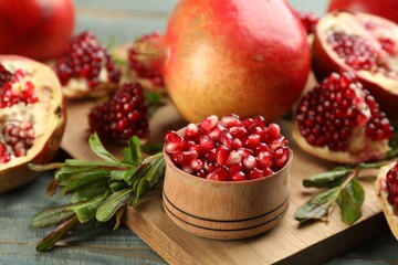 Delicious ripe pomegranate kernels in bowl on wooden board, closeup