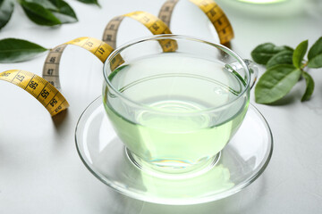 Cup of herbal diet tea and measuring tape on light table