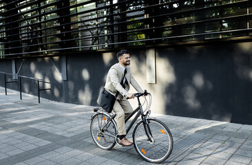Businessman riding bicycle in front of modern office building.