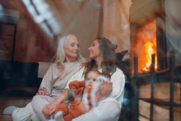 Grandmother, Mother and child sitting and playing on sofa near fireplace. Mom and baby. Parent with...