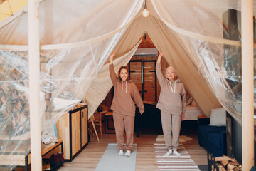 Family doing warming up exercises sports idoors. Young and senior elderly woman relaxing at glamping camping tent. Mother and daughter modern at fitness vacation lifestyle concept
