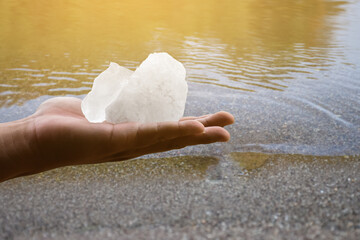 White alum bar holding in hand with cloudy water, concept for using alum to sway or swing the cloudy water to be clean and clear before using it in human daily life, soft and selective focus.