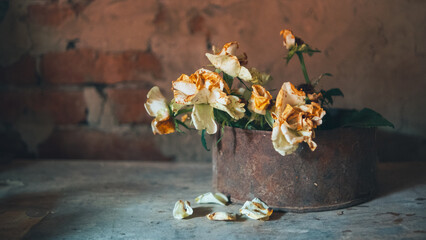 A bouquet of white fading roses in an old rusty iron jar against the background of a plastered brick wall, puzzles are scattered on the table
