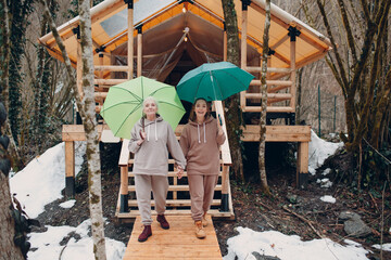 Elderly and young adult women with umbrella at glamping camping tent. Modern vacation lifestyle concept