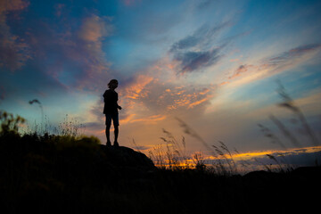 The silhouette of a human figure on a hill against the stunning beauty of the evening multicolored sky