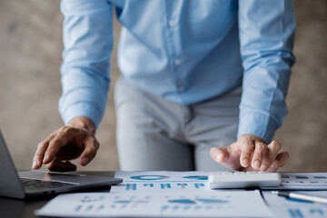 Businessman is using a calculator to calculate company financial figures from earnings papers, a businessman sitting in his office where the company financial chart is placed. Banner with copy space.