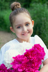 Fototapeta premium A beautiful little girl with a bouquet of peonies in her hands in a summer field. Photo shoot in the spring garden under the open sky.