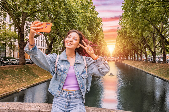 Happy girl travel blogger takes selfie pictures on her smartphone of the famous Konigsallee canal in the old town of Dusseldorf, Germany. Travel and sightseeing locations