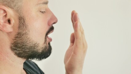 Bad breath. The concept of halitosis. A young man checks his breath with his hand