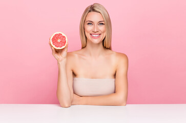 Obraz na płótnie Canvas Photo of positive lady sit podium hold orange ripe anti wrinkles dark spots treatment isolated over pastel pink color background