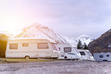 Caravan/motorhome against a wild backdrop of snow-capped mountains, with atmospheric glow effect  - obrazy, fototapety, plakaty