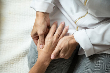 Closeup de mãos de massagista, que está ajoelhada no chão, aplicando massagem terapêutica na mão de um paciente que está deitada.