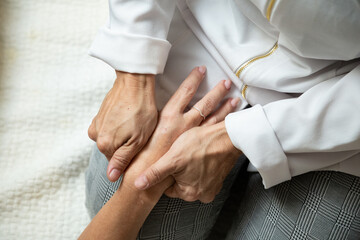 Closeup de mãos de massagista, que está ajoelhada no chão, aplicando massagem terapêutica na mão de um paciente que está deitada.