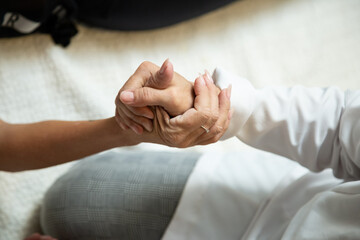 Closeup de mãos de massagista, que está ajoelhada no chão, aplicando massagem terapêutica na mão de um paciente que está deitada.