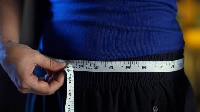 A young female measuring her waist with a tape measure - inch tape  weight loss  measuring tape  weight loss  . A young woman in exercise clothes standing with a tapeline - fitness and slimming  fi...