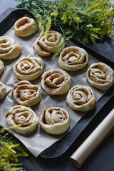  Unbaked cinnamon dough buns on a baking sheet  with yellow flowers and cooking paper, flatlay