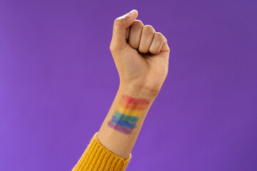 Close up of biracial man raising fist with lgbt flag on arm on purple background