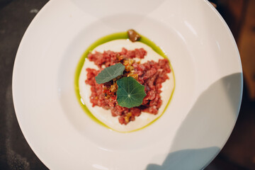 beef tartare on a large round plate with seasonal herbs and olive oil top view.