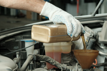 Maintenance of a passenger car in a service center. Oil change in the internal combustion engine. An auto mechanic holds a canister with his hand and pours oil into the engine compartment.