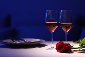 Beautiful table setting with glasses of wine and rose in dark room. Romantic dinner for Valentine's day