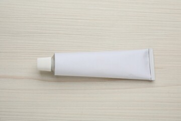 Blank white tube of ointment on light wooden table, top view. Space for text