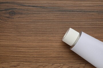 Blank white tube of ointment on wooden table, top view. Space for text