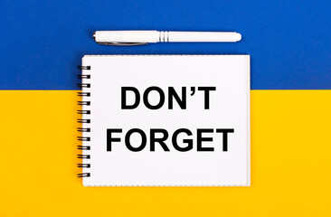 A white notebook with the text DO NOT FORGET and a white pen on a blue and yellow background.
