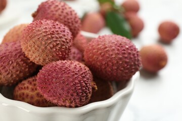 Fresh ripe lychee fruits in ceramic bowl on table, closeup