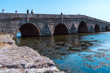 old stone bridge over river, historical bridge, people walking on,  mucilage on the river surface
