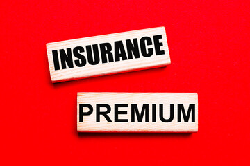 On a bright red background, there are two light wooden blocks with the text INSURANCE PREMIUM