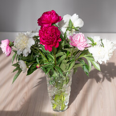 Ornate bouquet of various peonies in transparent vase located on the floor. Blurred room in background.