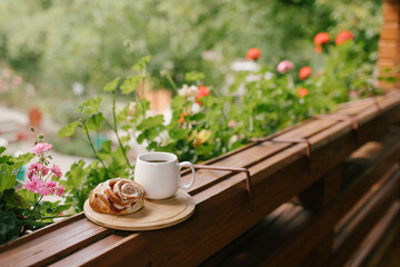 Mug with tea and cinnabon on tray on cozy balcony of wooden cottage.
