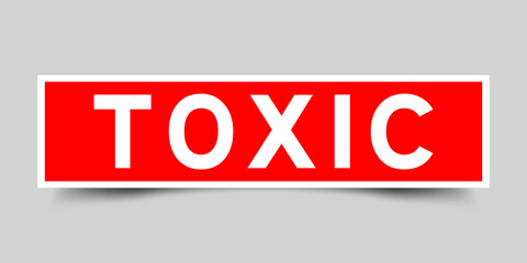 Red color square shape sticker label with word toxic on gray background