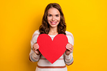 Portrait of pretty positive girl toothy smile arms hold heart postcard isolated on yellow color background