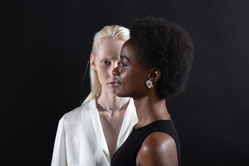 Caucasian albino girl and african american young woman portrait profile and full face on black background. Women friendship, love and relationships concept. - obrazy, fototapety, plakaty
