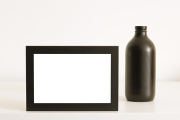 old black wooden blank frame and glass bottle on white table