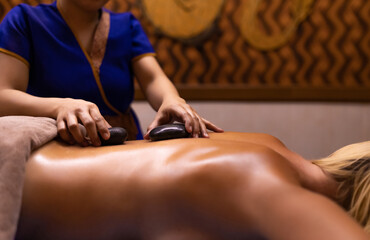 A masseur doing a hand and arm massage to adult woman with hot stones in her back. Massage treatment in spa salon.
