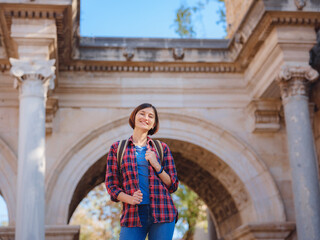travel to Turkey. Happy asian female tourist traveller with backpack walks in old city. Woman against backdrop of Hadrian's gate - popular attraction in old city of Antalya