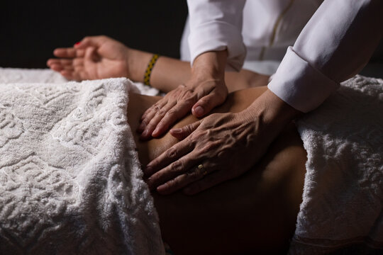 Closeup de m&atilde;os de massoterapeuta aplicando massagem terap&ecirc;utica na barriga de uma paciente.