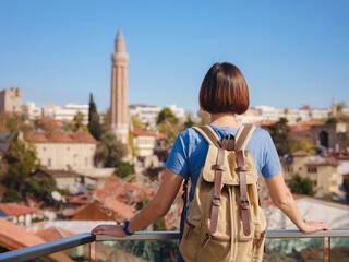 travel to Turkey, old town Antalya Kaleci. Happy asian female tourist traveller with backpack walks in old city. Woman on lookout over the old town and the port from viewpoint