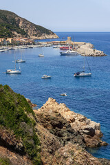 Vertical shot of coastal rocks of Elba Island covered with moss, white yachts moored in Marciana...