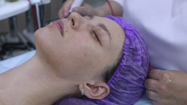 Beautician using electrical impulses for facial procedures. Microcurrent massage. The hands of a beautician spend electrodes around the eyes of a young woman. Apparatus cosmetology.