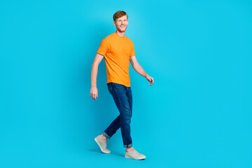 Fototapeta na wymiar Full size profile photo of cheerful ginger hair guy go wear t-shirt jeans shoes isolated on blue color background