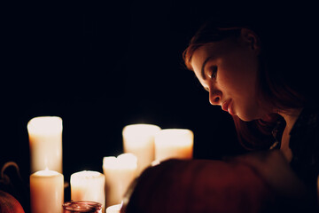 Young woman making Halloween pumpkin Jack-o-lantern with candles in dark. Female hands cutting...