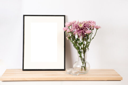 A mock-up of a black photo frame on wooden table, a transparent vase with pink summer flowers