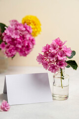Blank white paper greeting card mock up. Pink and yellow flowers in vases with copy space. Hydrangea, dahlias and eucalyptus.