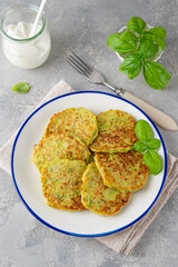 Zucchini fritters with cheese, garlic and herbs. Vegetarian zucchini pancakes, served with basil and sour cream on a gray concrete background. Selective focus.