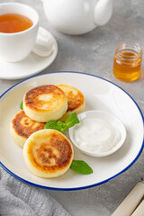 Cottage cheese pancakes, syrniki, ricotta fritters with honey and sour cream on a gray concrete background. Healthy and delicious breakfast. Top view, copy space.